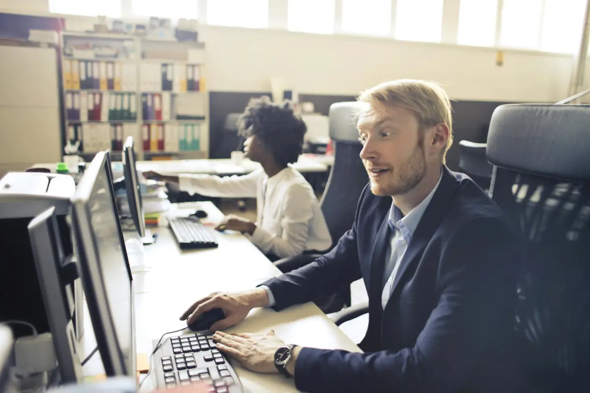 An image of 2 workers working in an office with computers